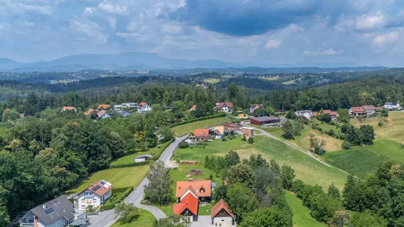 Luftaufnahme einer hügeligen Landschaft mit Wohnhäusern, Straßen und weiten Waldgebieten.
