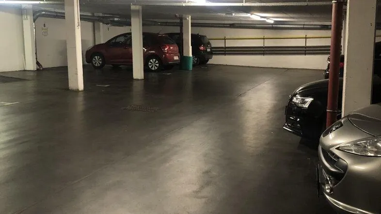 Geräumige Tiefgarage mit mehreren geparkten Fahrzeugen, Betonpfeilern und heller Deckenbeleuchtung.