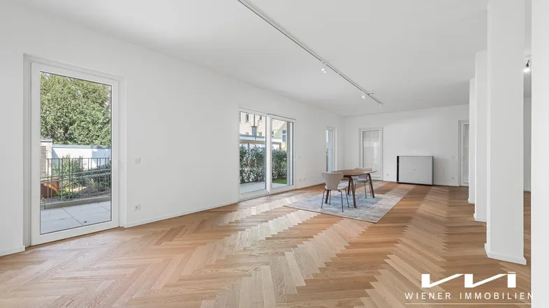 Heller, offener Wohnbereich mit Fischgrätparkett, großen Fenstern und Zugang zu einer Terrasse.
