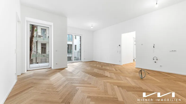 Helles Wohnzimmer mit Fischgrätparkett und Zugang zu einem französischen Balkon.