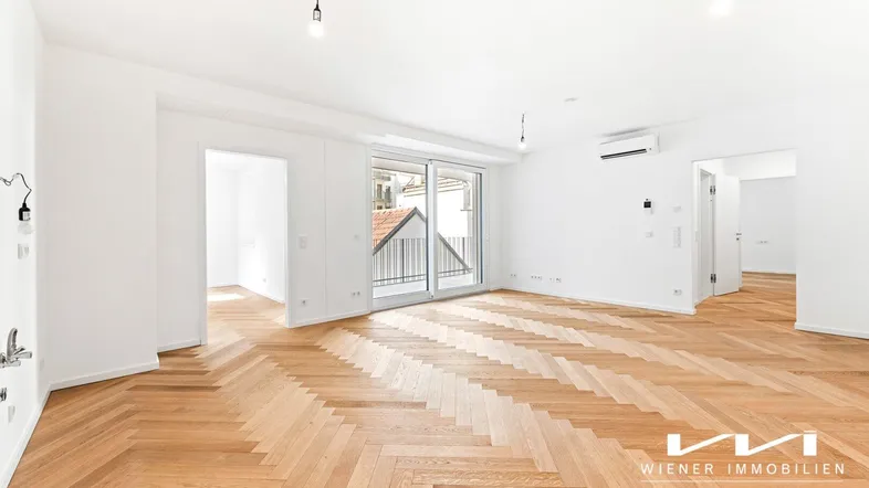 Heller Wohnraum mit elegantem Fischgrätparkett, weißen Wänden und Zugang zu einem Balkon.
