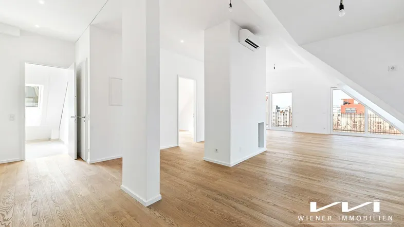Geräumiger, heller Wohnbereich im Dachgeschoss mit Holzboden, hohen Decken und Zugang zu einem Balkon.