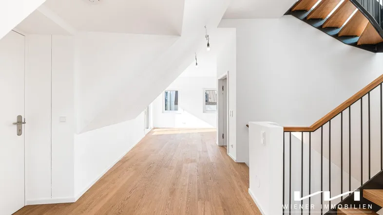 Heller Flur mit Holzparkettboden, Dachschrägen und moderner Treppe, die zu weiteren Räumen führt.