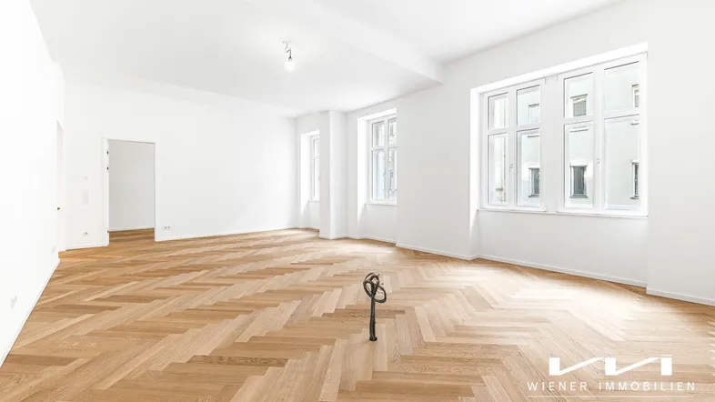 Helles, geräumiges Zimmer mit Fischgrätparkett und großen Fenstern, ideal als Wohnbereich.