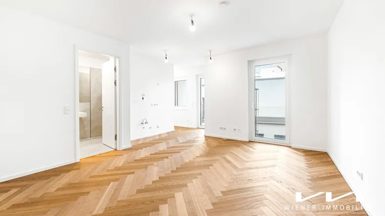 Helles, leeres Zimmer mit Fischgrätparkett und Zugang zu einem Balkon oder einer Terrasse.