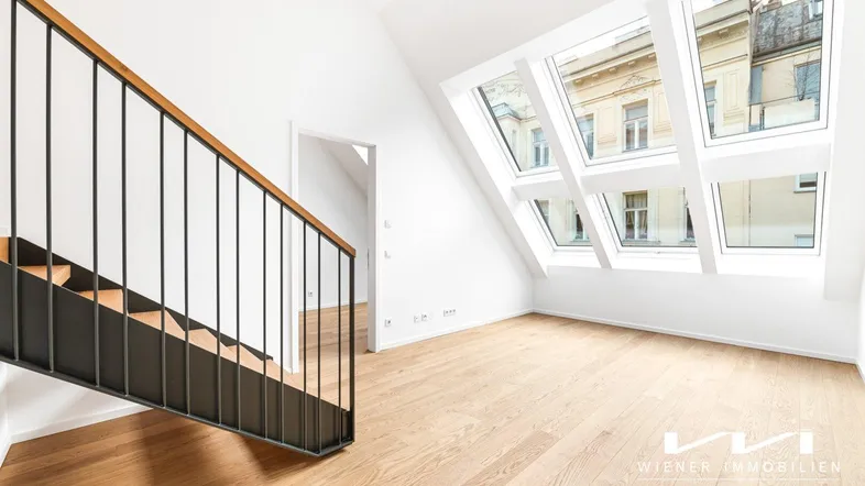 Helles Dachgeschosszimmer mit Holzfußboden, moderner Treppe und großen Dachfenstern.