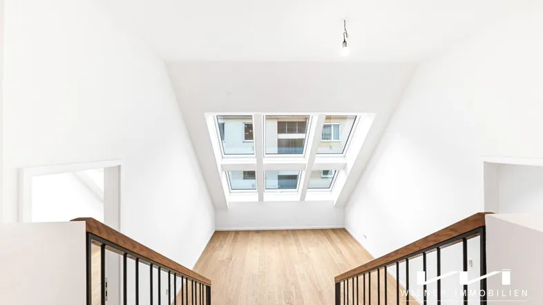 Heller Dachbodenbereich mit großen Dachfenstern, Holzfußboden und moderner Treppe.