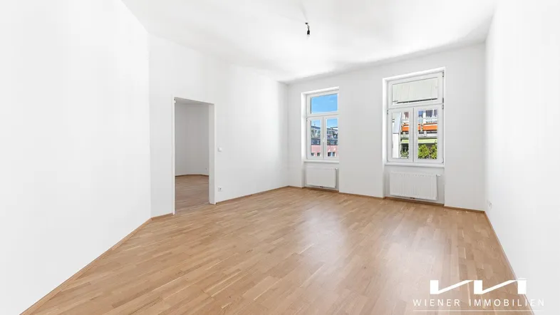 Helles, leeres Zimmer mit Parkettboden und zwei Fenstern, bereit zur individuellen Gestaltung.