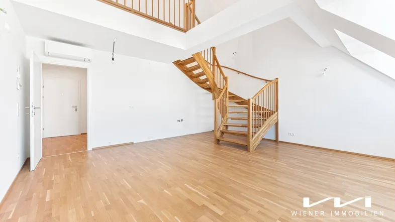 Heller Wohnraum mit Holztreppe, Dachschrägen und Parkettboden, der zu einer oberen Ebene führt.