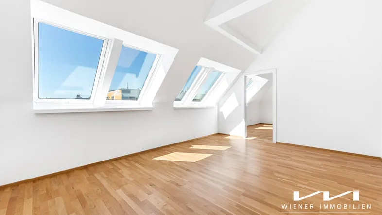 Helles Dachzimmer mit Holzboden und mehreren Dachfenstern, die viel Tageslicht hereinlassen.