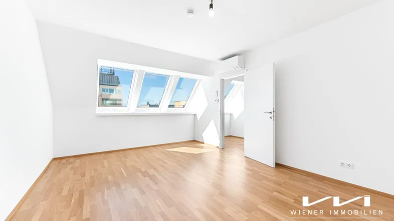 Helles Zimmer im Dachgeschoss mit Holzparkettboden, Dachfenstern und Klimaanlage.