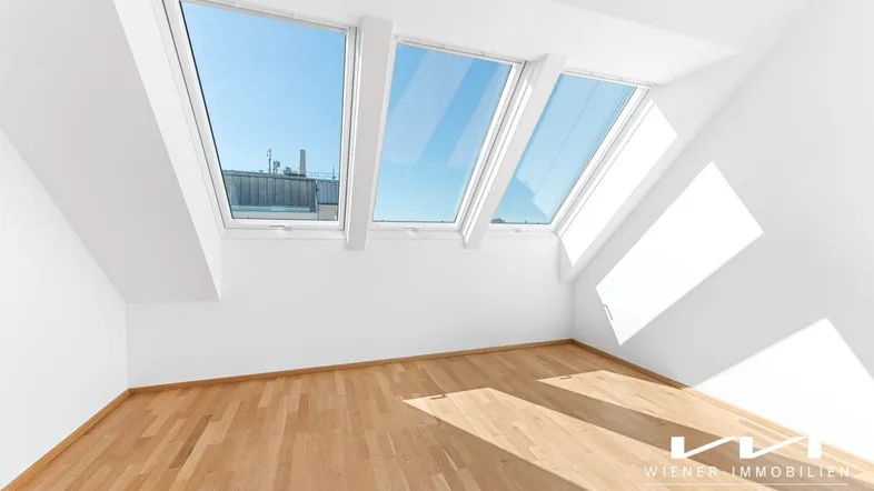 Heller Raum im Dachgeschoss mit Holzboden und drei großen Dachfenstern, die viel Licht hereinlassen.