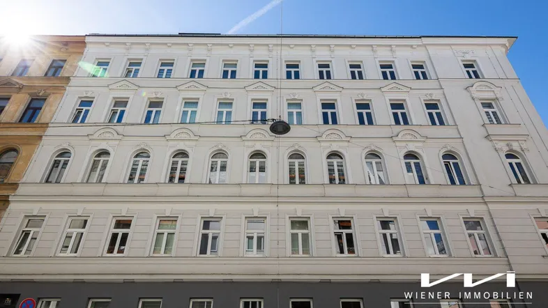 Klassische Fassade eines Mehrfamilienhauses mit vielen Fenstern unter strahlend blauem Himmel.