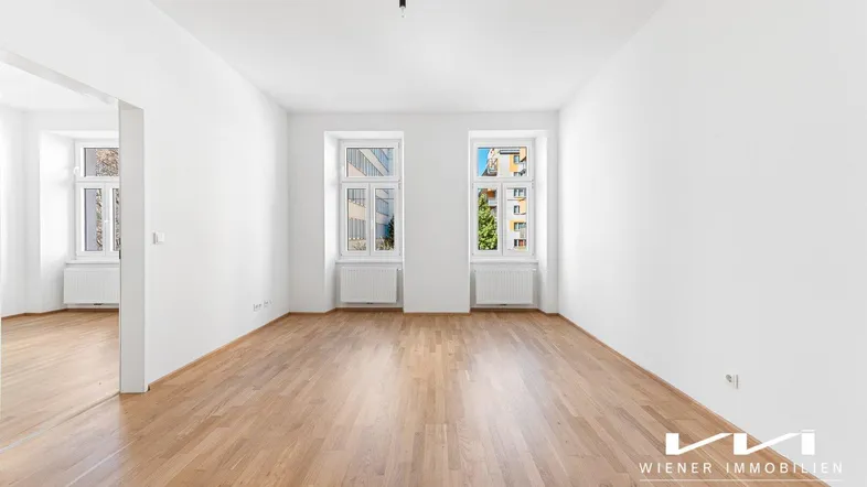 Helles, leeres Zimmer mit Parkettboden und zwei großen Fenstern, bereit zur individuellen Gestaltung.