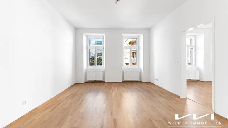 Helles, leeres Zimmer mit Parkettboden und zwei großen Fenstern, bereit zur individuellen Gestaltung.