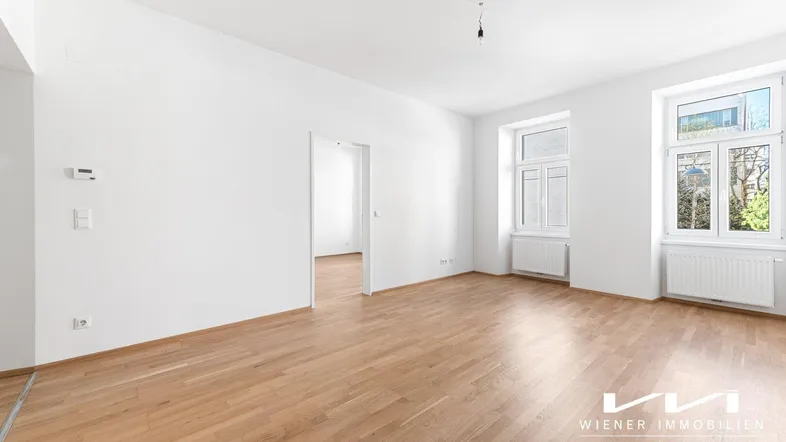 Helles, leeres Zimmer mit Parkettboden und großen Fenstern, bereit für individuelle Gestaltung.