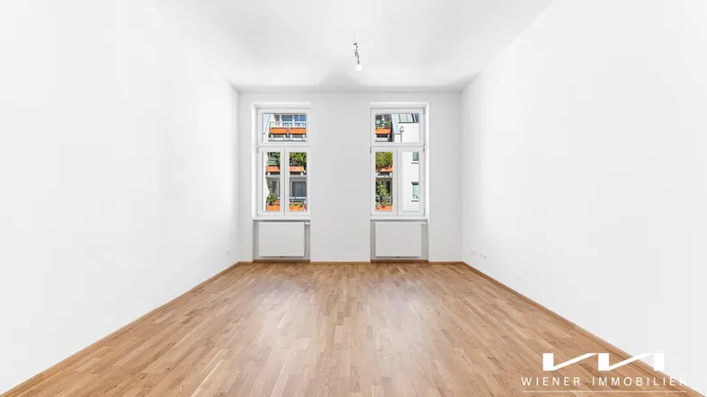 Helles, leeres Zimmer mit frisch verlegtem Parkettboden und zwei Fenstern, bereit zur individuellen Gestaltung.