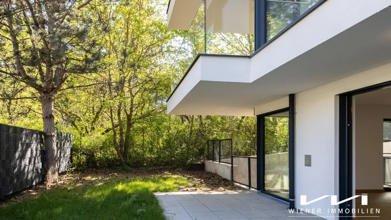 Moderne Architektur mit großer Terrasse, Rasenfläche und viel Grün in sonniger Umgebung.