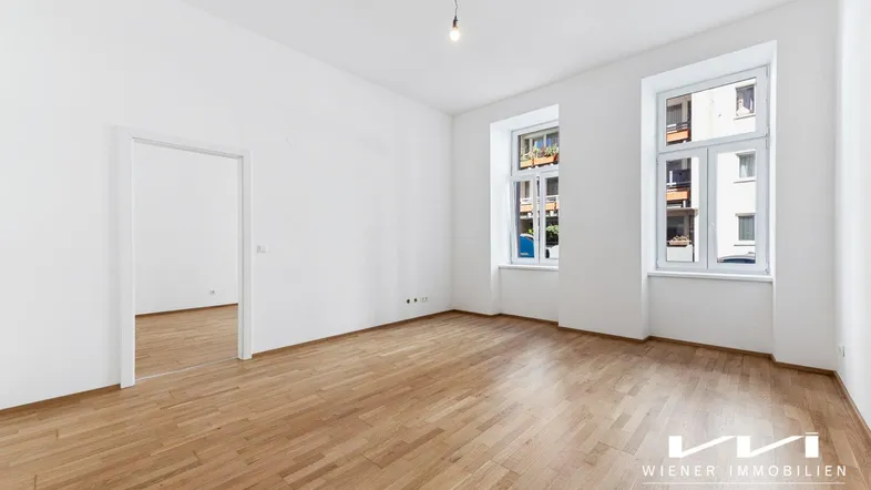 Helles, unmöbliertes Zimmer mit Parkettboden, hohen Decken und zwei großen Fenstern.