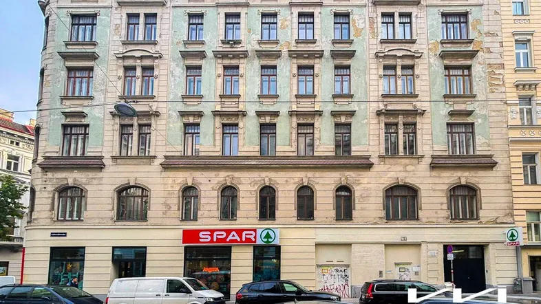 Altes Mehrfamilienhaus mit klassischer Fassade und einem Supermarkt im Erdgeschoss an einer Stadtstraße.
