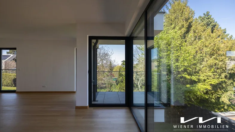 Helles Wohnzimmer mit großen Glasfronten, Holzboden und Zugang zu einem Balkon.