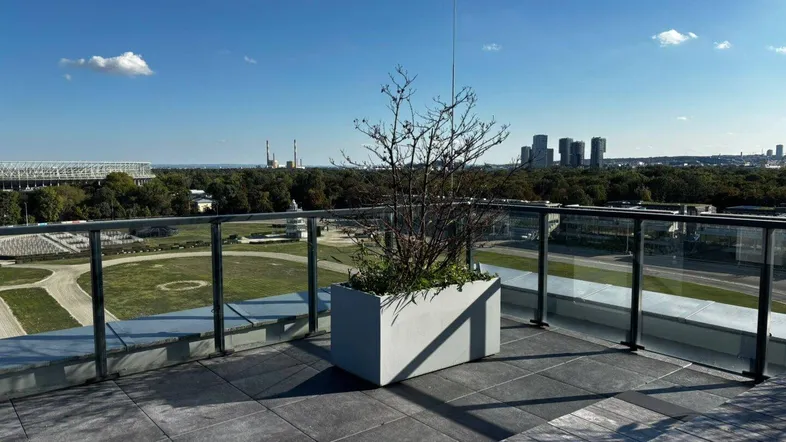Große Dachterrasse mit modernen Fliesen, Glasgeländer und weitem Blick über die Stadt.