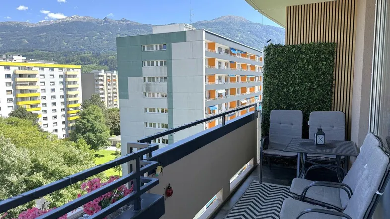 Gemütlicher Balkon mit Sitzgruppe und Blick auf die Stadt und die majestätischen Berge.