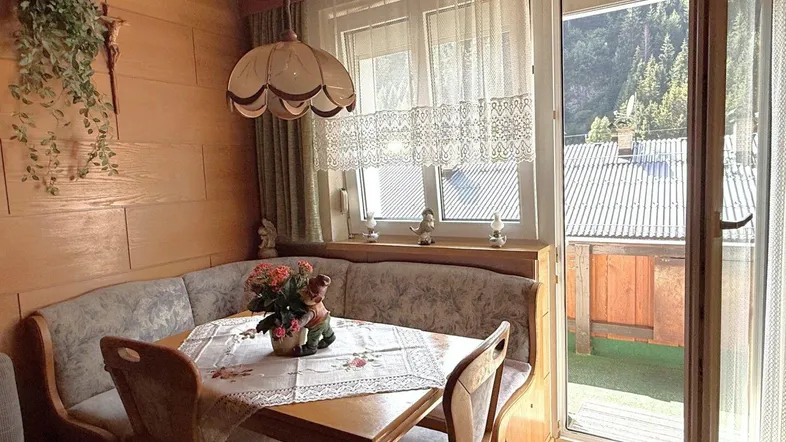 Gemütliche Essecke mit traditioneller Eckbank und Blick durch die Balkontür auf die Umgebung.
