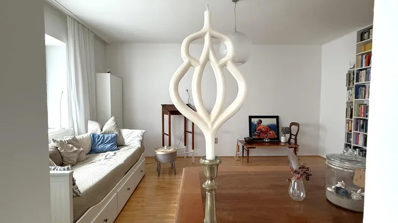 Helles Wohnzimmer mit Holzboden, Tagesbett und Bücherregal, durch einen Durchgang sichtbar.