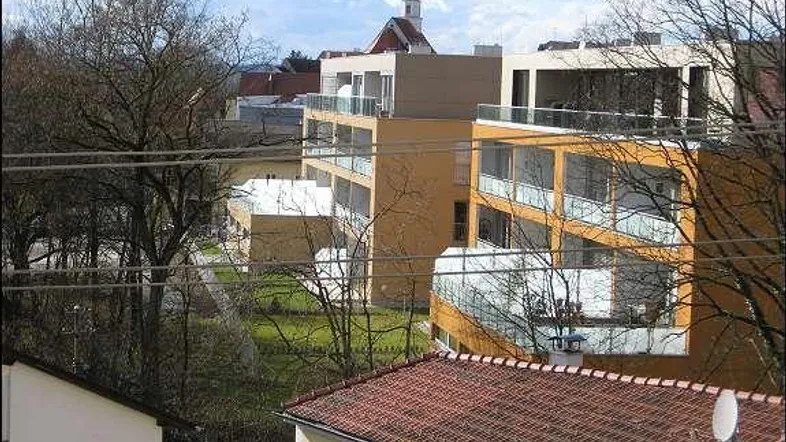 Blick auf moderne Mehrfamilienhäuser mit Balkonen und Grünflächen, im Hintergrund ein Kirchturm.