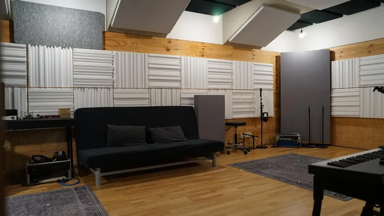 Geräumiges Tonstudio mit akustischen Paneelen, Holzwänden und einem bequemen Sofa für Aufnahmen.