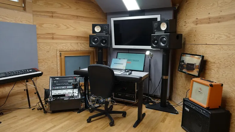 Professionelles Musikstudio mit Holzwänden, Schreibtisch, Monitoren und umfangreicher Audioausrüstung.