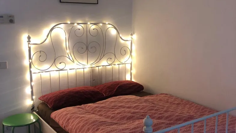 Gemütliches Schlafzimmer mit romantischer Lichterkette am verzierten Metallbett und dunklem Holzboden.