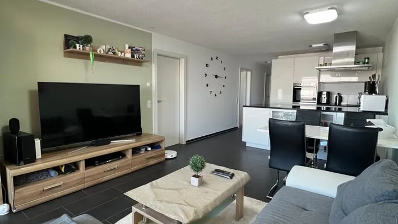 Moderner offener Wohnbereich mit integrierter Küche, dunklen Fliesen und hellem Sofa.