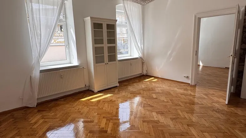 Lichtdurchflutetes Wohnzimmer mit Fischgrätparkett, hohen Decken und elegantem Kronleuchter.