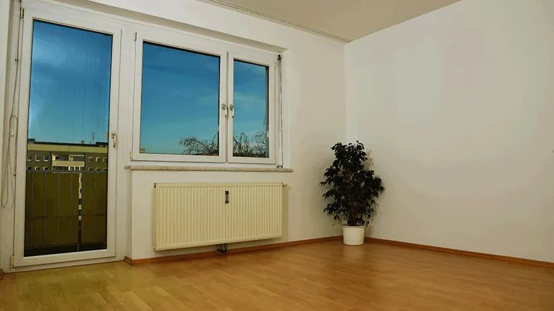 Helles Zimmer mit Parkettboden, großem Fenster und Zugang zu einem französischen Balkon.