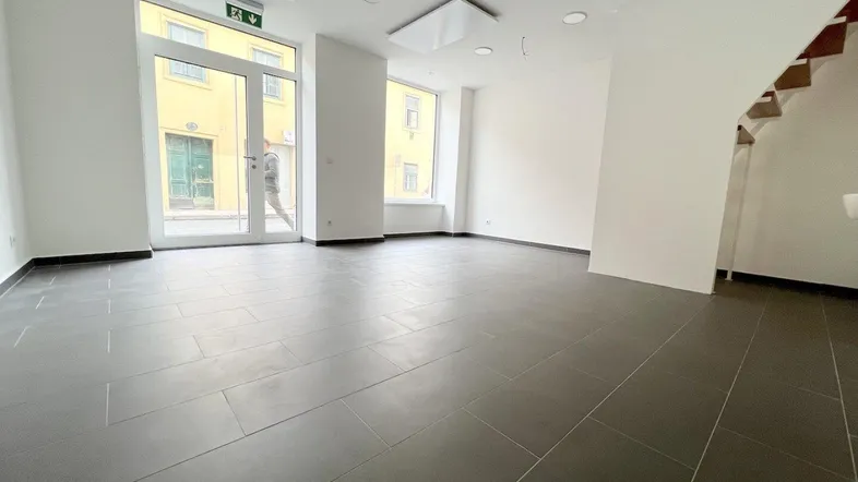 Modernes, helles Ladenlokal mit großen Fenstern und dunklen Fliesen in makellosem Zustand.