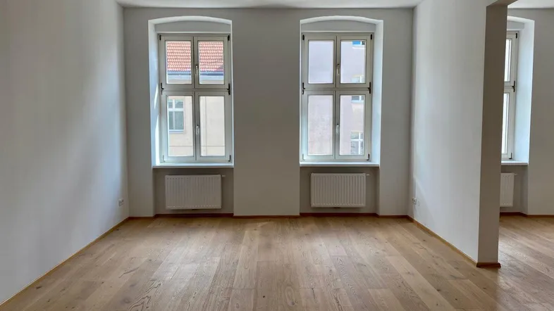 Helles, leeres Zimmer mit Holzboden und zwei Fenstern, bereit zur individuellen Gestaltung.