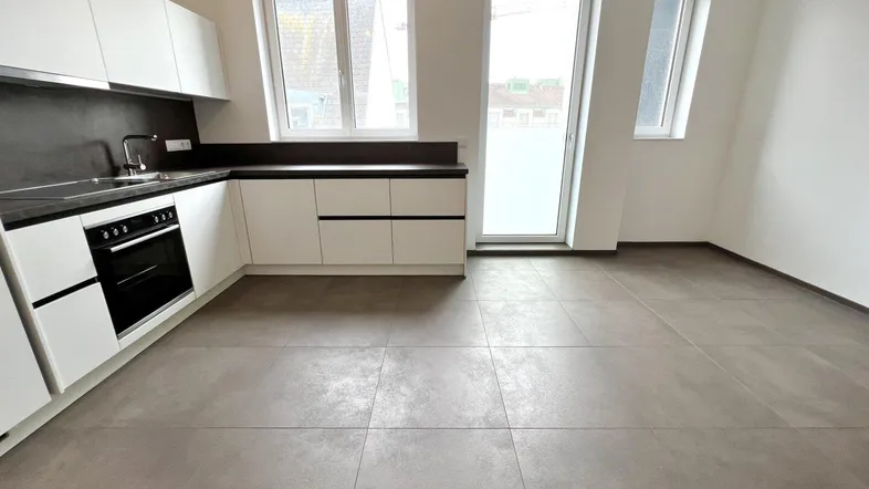 Moderne Küche mit weißen Schränken, dunkler Arbeitsplatte, integriertem Backofen und großen Fliesen.
