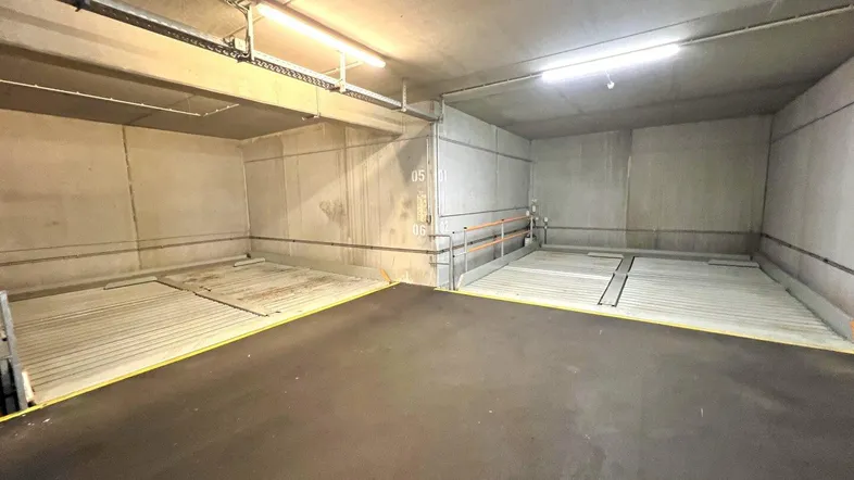 Tiefgarage mit zwei Doppelparkern und robusten Betonwänden, beleuchtet von Neonröhren.