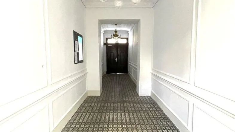Langer Flur mit gemustertem Fliesenboden, Stuckdecke und klassischer Deckenleuchte in einem Altbau.