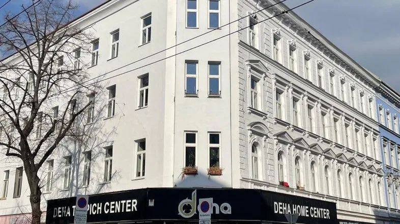 Weißes Eckgebäude mit Geschäften im Erdgeschoss und traditioneller Architektur in der Stadt.