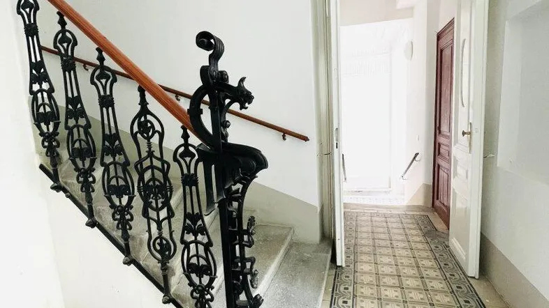 Historisches Treppenhaus mit kunstvollem Geländer und gemusterten Fliesen im Eingangsbereich des Gebäudes.