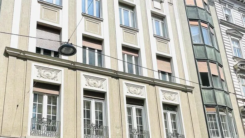 Klassisches Gebäude mit mehreren Stockwerken, verzierten Fenstern und Rollläden an der Fassade.