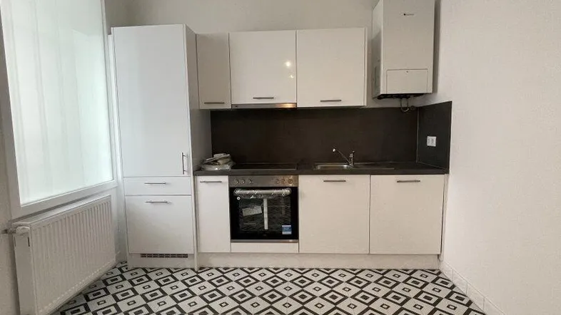 Moderne Küche mit weißen Schränken, dunkler Arbeitsplatte und auffälligem schwarz-weißem Fliesenboden.