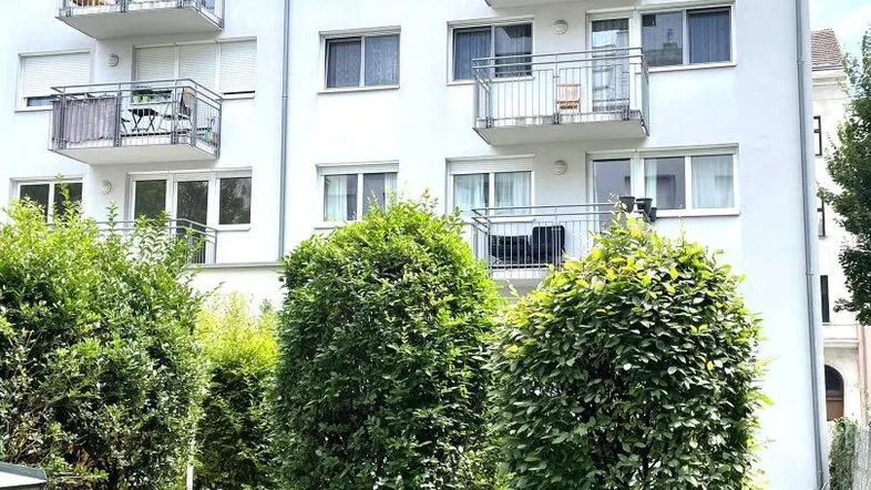 Weißes Mehrfamilienhaus mit mehreren Balkonen und gepflegten Grünflächen im Vordergrund.