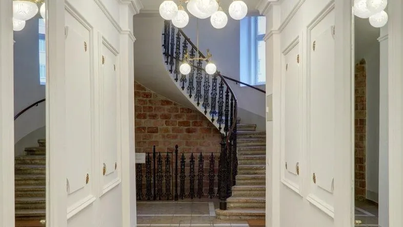 Eleganter Flur mit Stuckdecke, Kronleuchter und einer geschwungenen Treppe im Hintergrund.