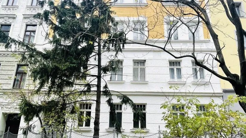Klassisches Mehrfamilienhaus mit weißer und gelber Fassade und Bäumen davor.