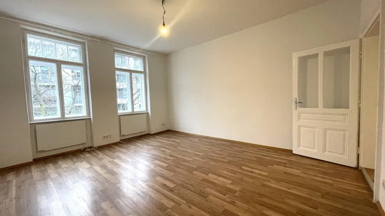 Heller Raum mit Parkettboden, weißen Wänden und großen Fenstern, ideal als Wohnzimmer.