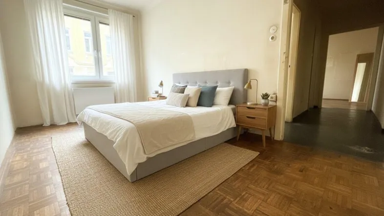 Helles Schlafzimmer mit modernem Bett, Holzboden und Blick auf die Stadt.